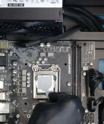 Mão com luva preta aplicando pasta térmica no processador de uma placa-mãe, na bancada da Benincasa Info